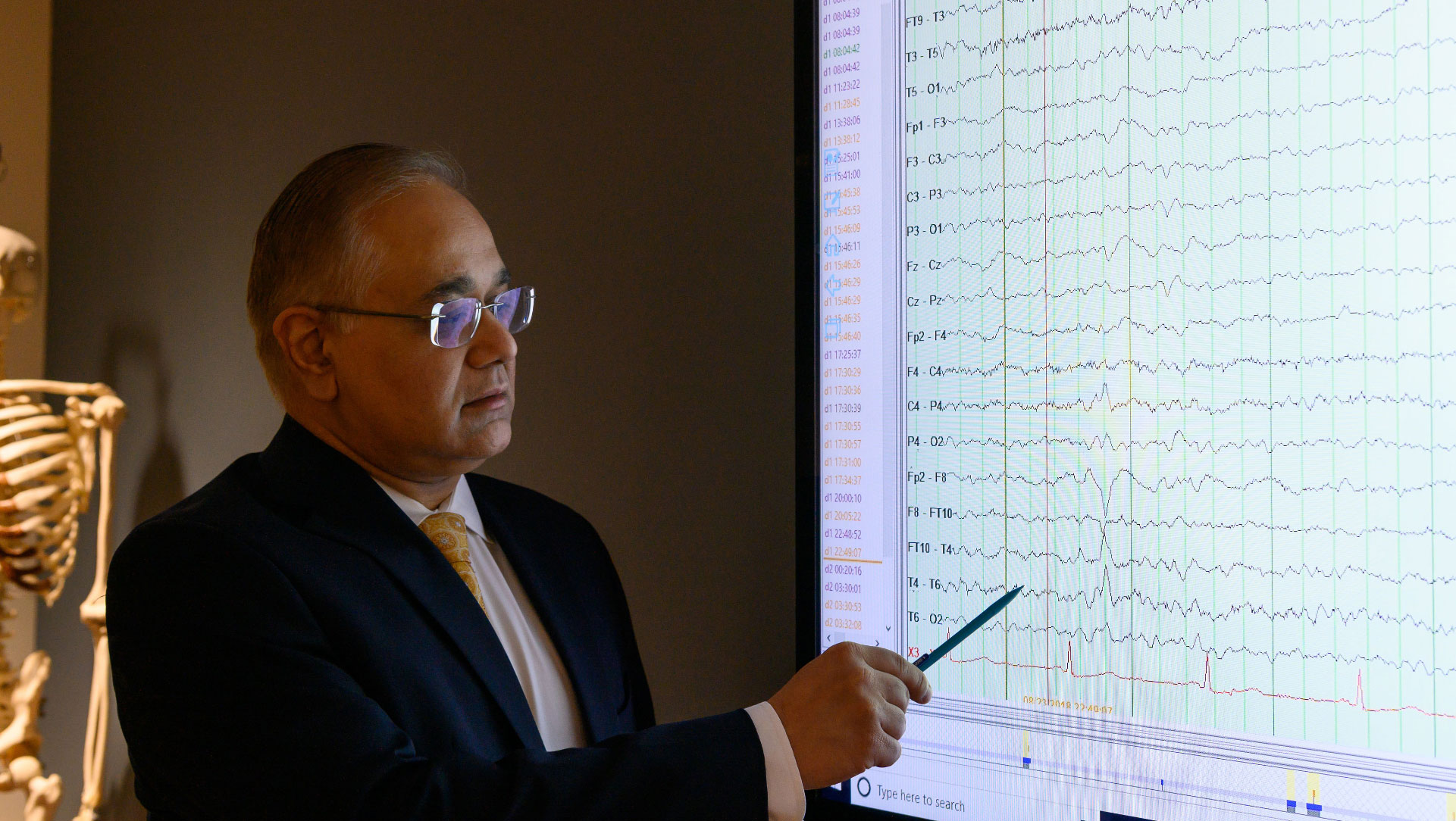 Dr. Siddharth Kapoor, pictured in a dark room looking at a projector screen displaying monitor scans while he points at the screen with a pen.