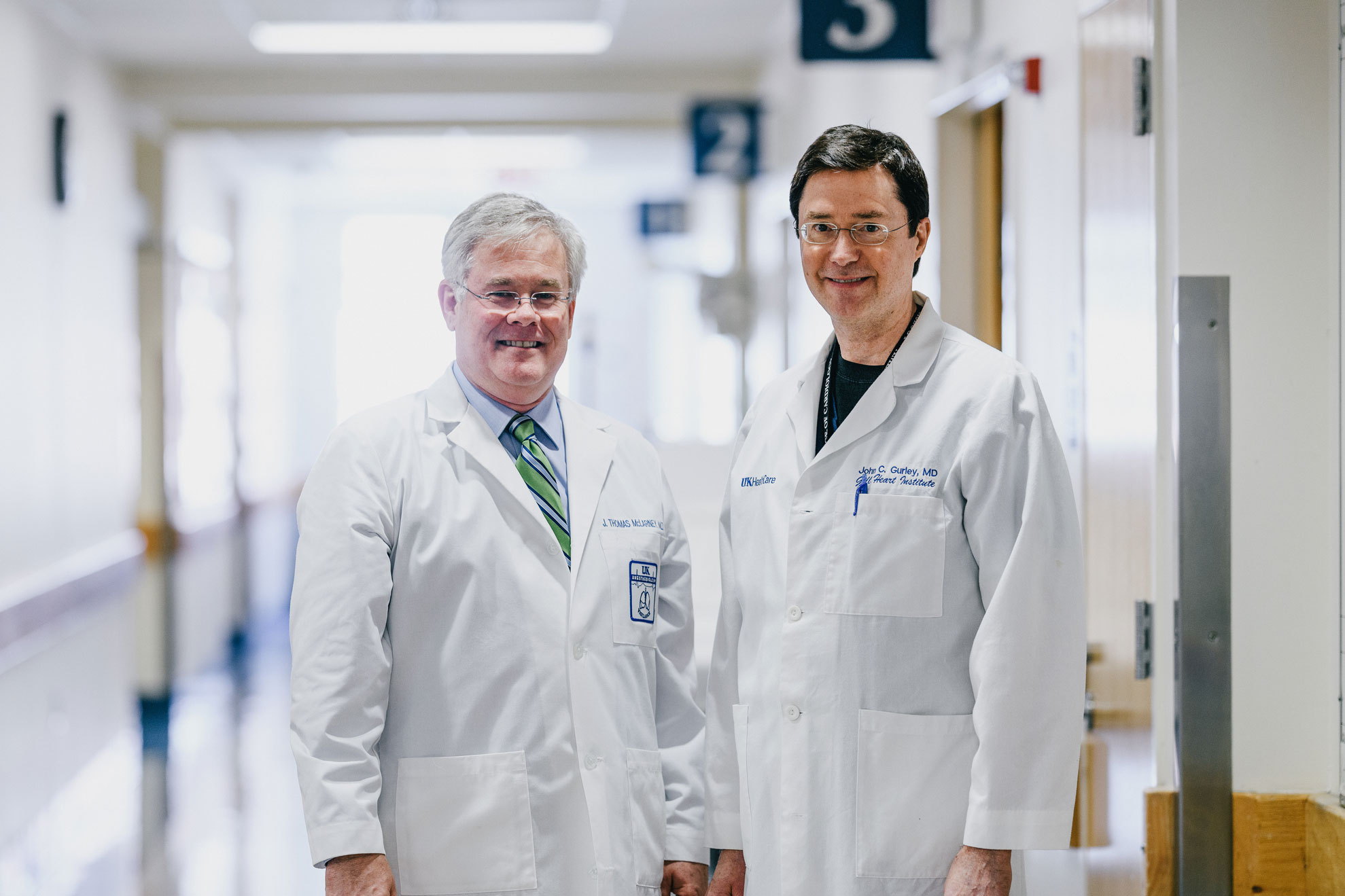 Dr. McLarney and Dr. Gurley wearing their white doctor's coats smile for a photo in a hallway at the hospital.