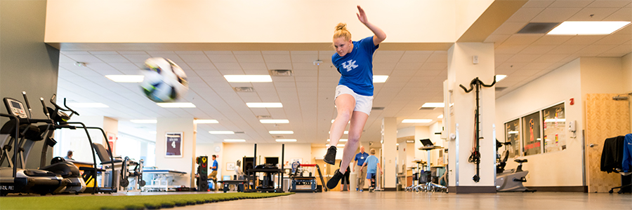 A foot and ankle patient kicks a soccer ball in the physical therapy room.